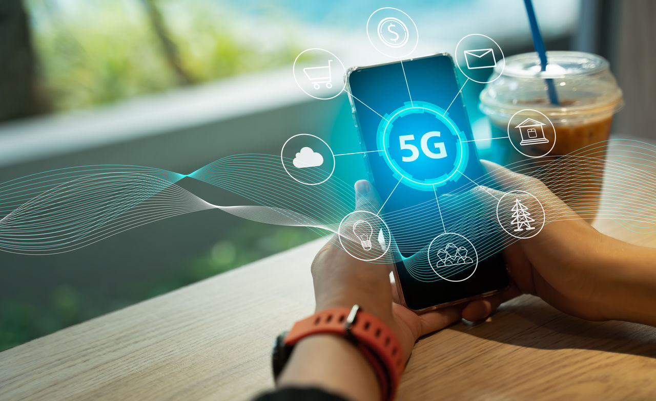 Close up of female hand holding a phone with a 5G hologram in coffee shop. 5G network wireless systems.The concept of 5G network, high-speed mobile Internet, new generation networks.