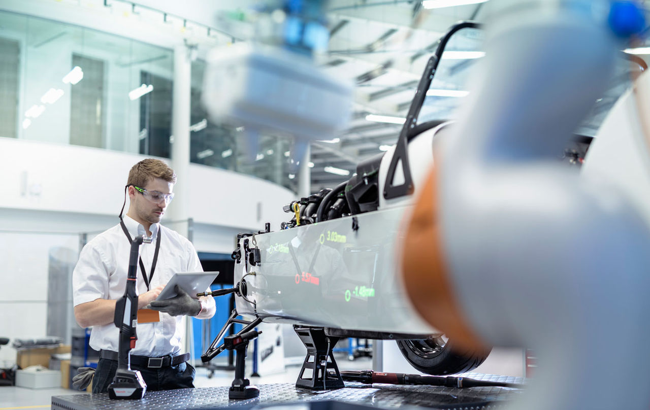 A manufacturing employee inspecting a vehicle on a production line using a tablet.