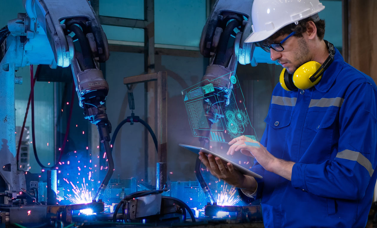 An industrial technician utilizing augmented reality (AR) technology to monitor or control robotic arms.